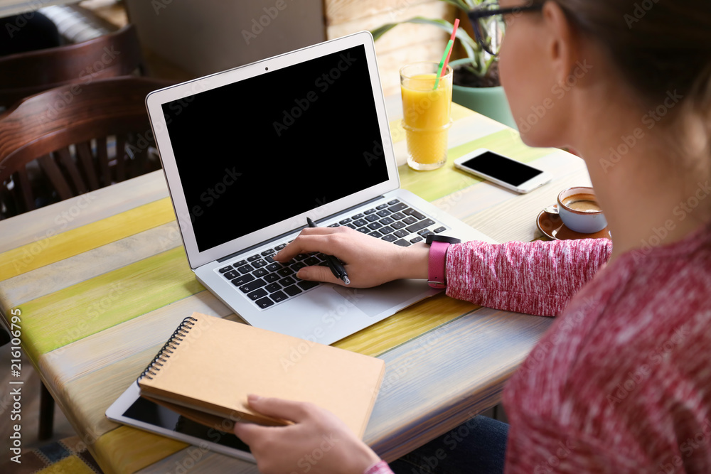 Young freelancer with laptop working and notebook in cafe