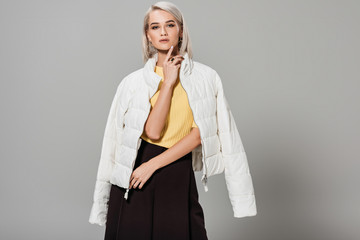 confident young female model in white jacket over shoulders posing isolated on grey background