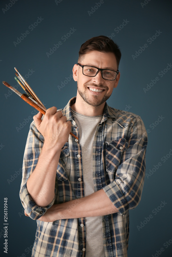 Male artist holding paintbrushes on color background