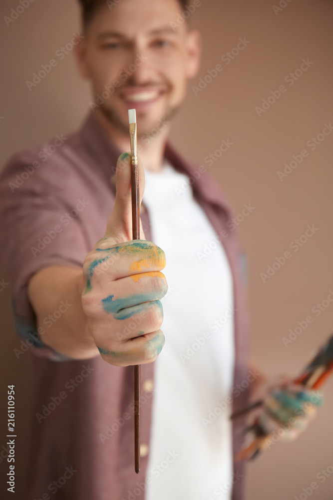 Male artist holding paintbrush on color background