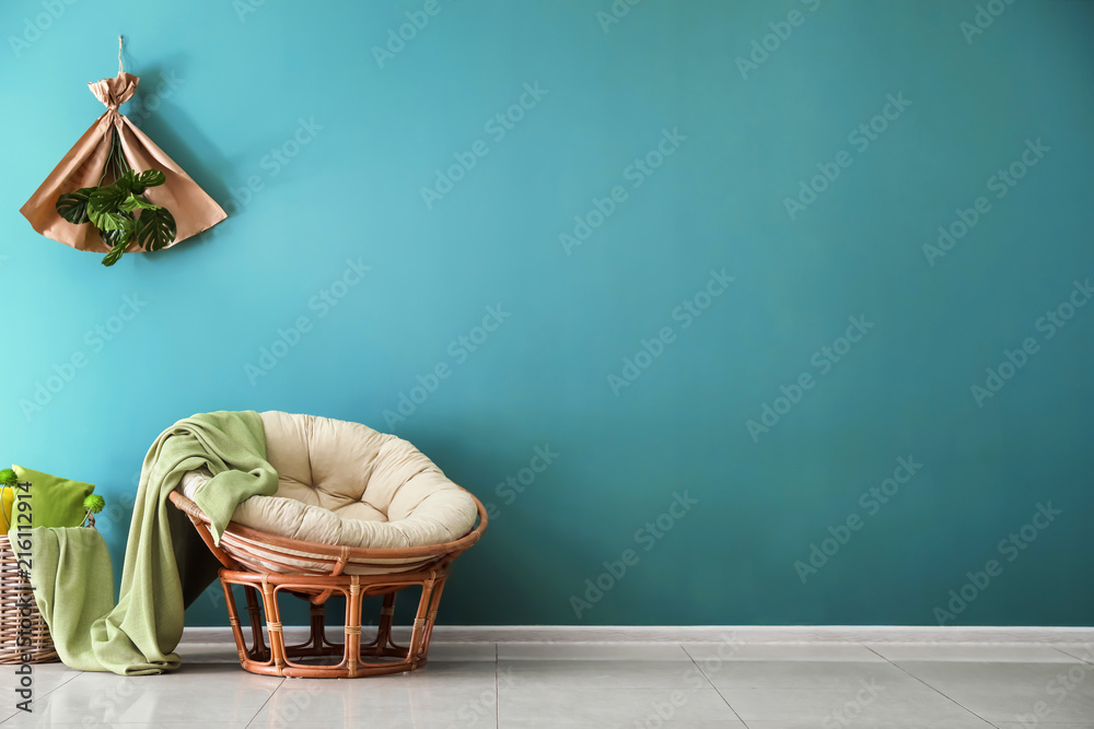 Comfortable armchair with wicker basket near color wall