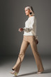 © LIGHTFIELD STUDIOS - fashionable girl walking in beige pants and white sweater, on grey