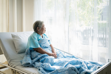 Asian depressed elderly woman patients lying on bed looking out the window in hospital. Elderly woman patients is glad recovered from the illness.