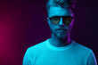 © monchak - Neon light studio portrait of serious man model with mustaches and beard in sunglasses and white t-shirt