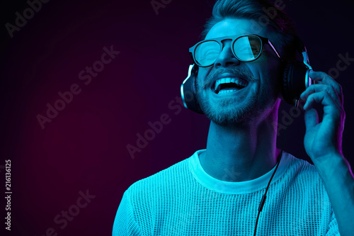 Photographie Neon portrait of bearded smiling man in headphones, sunglasses, white t-shirt