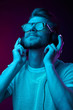 © monchak - Handsome man in glasses enjoys listening to music with headphones. Neon studio portrait