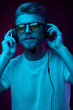 © monchak - Handsome man in glasses enjoys listening to music with headphones. Neon studio portrait