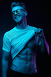 © monchak - Neon light portrait of sexy smiling man in yellow glasses, pulling up t-shirt, showing abs