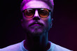 © monchak - Neon light close-up portrait of serious man model with mustaches and beard in sunglasses and white t-shirt