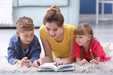 Wall Mural - Mother and her children reading book together at home