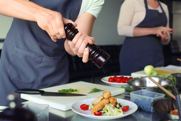 Chef preparing fried meat with salad for serving in restaurant kitchen