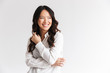 Photo of optimistic asian woman with long dark hair looking aside at copyspace and laughing, isolated over white background in studio
