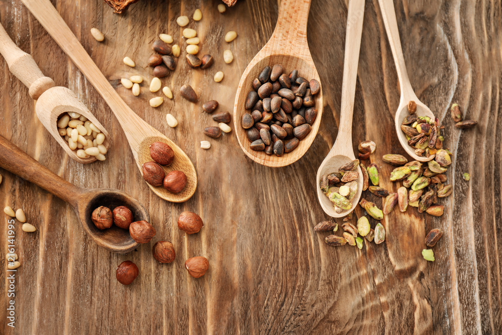 Spoons with different nuts on wooden background