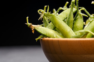 Photo of green pea pods in wooden plate on empty black background