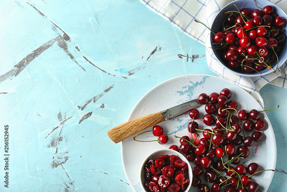 Bowls and plate with ripe cherries on color table
