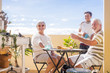 grandfathers adult mature and teenager nephew enjoy outdoor in the terrace some leisure with food and drinks. ocean and city view, vacation sunny day nice weather concept and background. happy people