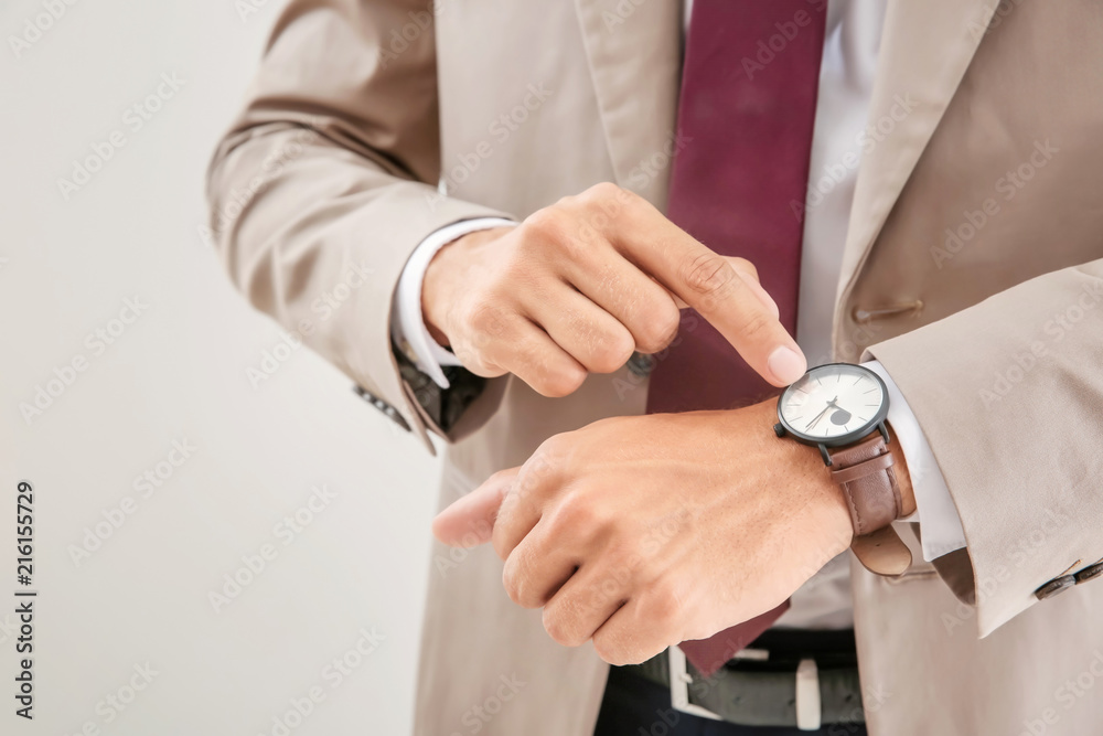 Businessman looking at his watch on light background, closeup. Time management concept