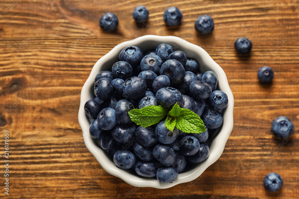 Bowl with ripe blueberries on wooden background