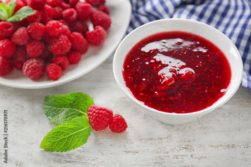 Bowl with tasty raspberry jam on wooden table