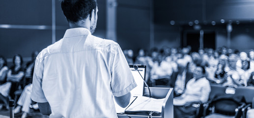 Speaker giving a talk on corporate business conference. Unrecognizable people in audience at conference hall. Business and Entrepreneurship event. Black and white, blue toned image.