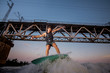 © fesenko - Active man jumping on wakesurf down the river waves against the bridge at the sunset
