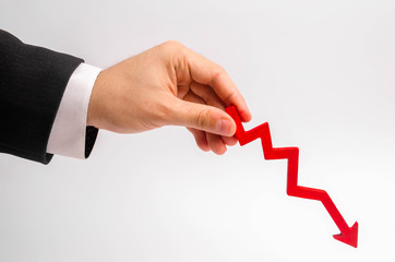 A businessman's hand is holding a red arrow down on a white background. The concept of reducing costs and profits, falling living standards and prices. Decreased projections, depressed economies.