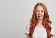 Portrait Of Cheerful Playful Young Woman With Long Wavy Red Hair And Freckles Wears T Shirt Winks And Shows Tongue Isolated Over White Background