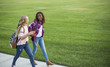 © Brocreative - Two diverse school kids walking and talking together on the way to school. Back to school photo of diverse girls wearing backpacks in the school yard