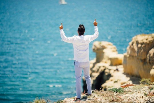 Rear view of Young handsome man pointed up or praying on ocean background