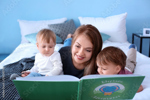 Cuadros en Lienzo Young nanny reading book to cute little children on bed