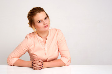 Portrait of a beautiful blond business girl on a white background sits at a table.