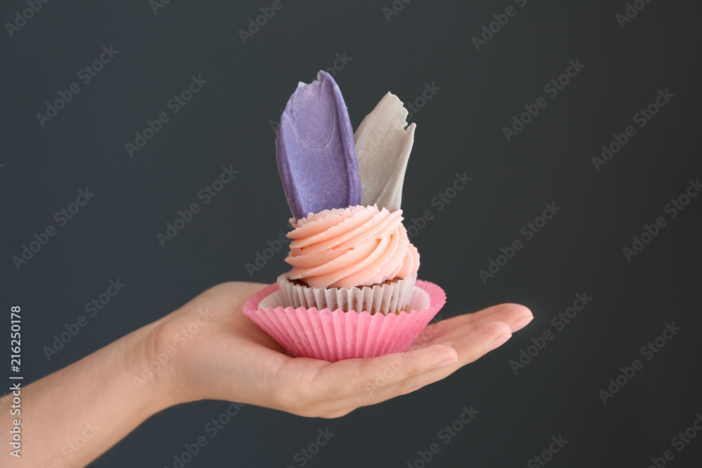 Female hand holding delicious birthday cupcake on dark background