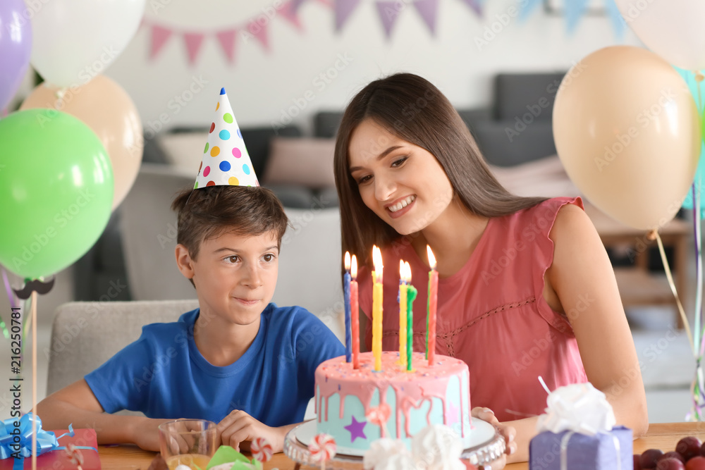 Cute little boy and his mother at table with birthday cake