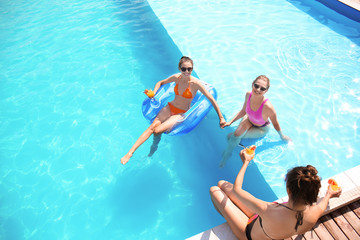 Wall Mural - Beautiful young women drinking cocktails in swimming pool on summer day