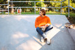 © Anton - Young guy in orange pullover and jeans holding bottle of water in hand while thoughtfully looking aside at skatepark