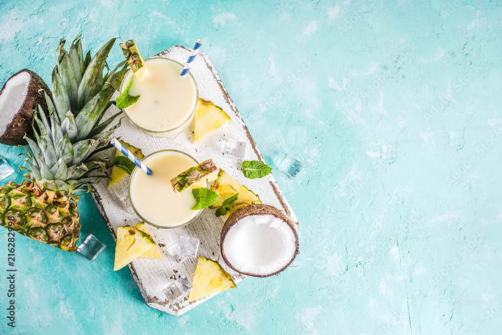 Refreshing summer drink, homemade pina colada cocktail, on a light blue background, with pieces of pineapple, coconut, ice and mint leaves, copy space top view - obrazy, fototapety, plakaty 