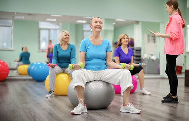 Sticker - Group of mature women with young coach training in modern gym