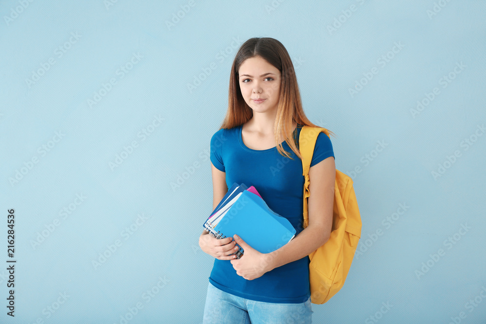 Teenage girl with backpack and notebooks on color background