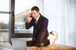 © Africa Studio - Young man in elegant suit talking on cell phone at workplace