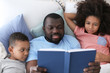 © Africa Studio - African American man reading bedtime story to his children in bed