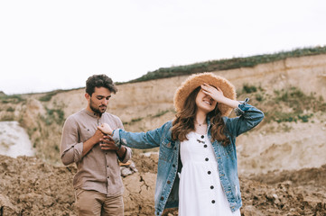 stylish girl closing eyes and holding hands with happy boyfriend in sand canyon