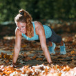 © Microgen - Woman doing push ups in the park, in the fall.