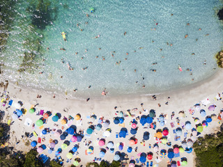 Wall Mural - View from above, aerial view of an emerald and transparent Mediterranean sea with a white beach full of colored beach umbrellas and tourists who relax and swim. Costa Smeralda, Sardinia, Italy.