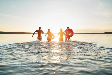 Friends running into a lake at sunset splashing water