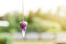 Purple Amethyst Crystal Pendulum On Chain, Outdoors Trees And Nature On The Background.