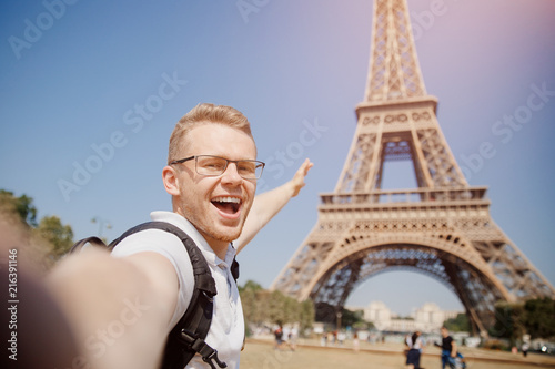 Foto Man tourist with backpack and wearing glasses makes selfie photo on background of Eiffel Tower in Paris, France