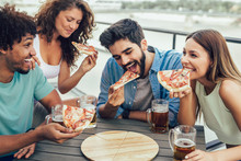 Friends Enjoying Pizza. Group Of Young Cheerful People Eating Pizza And Drinking Beer While Sitting At The Bean Bags On The Roof Of The Building