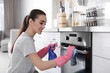 © New Africa - Young woman cleaning oven with rag in kitchen