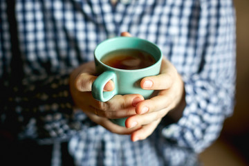 a young woman sits by the window and holds a mug with hot tea