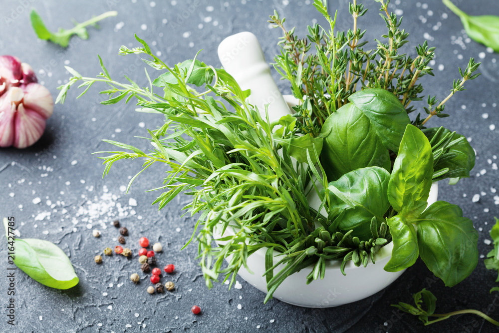 Fresh green garden herbs in mortar bowl and spices on black stone table. Thyme, rosemary, basil, and tarragon for cooking. - obrazy, fototapety, plakaty 